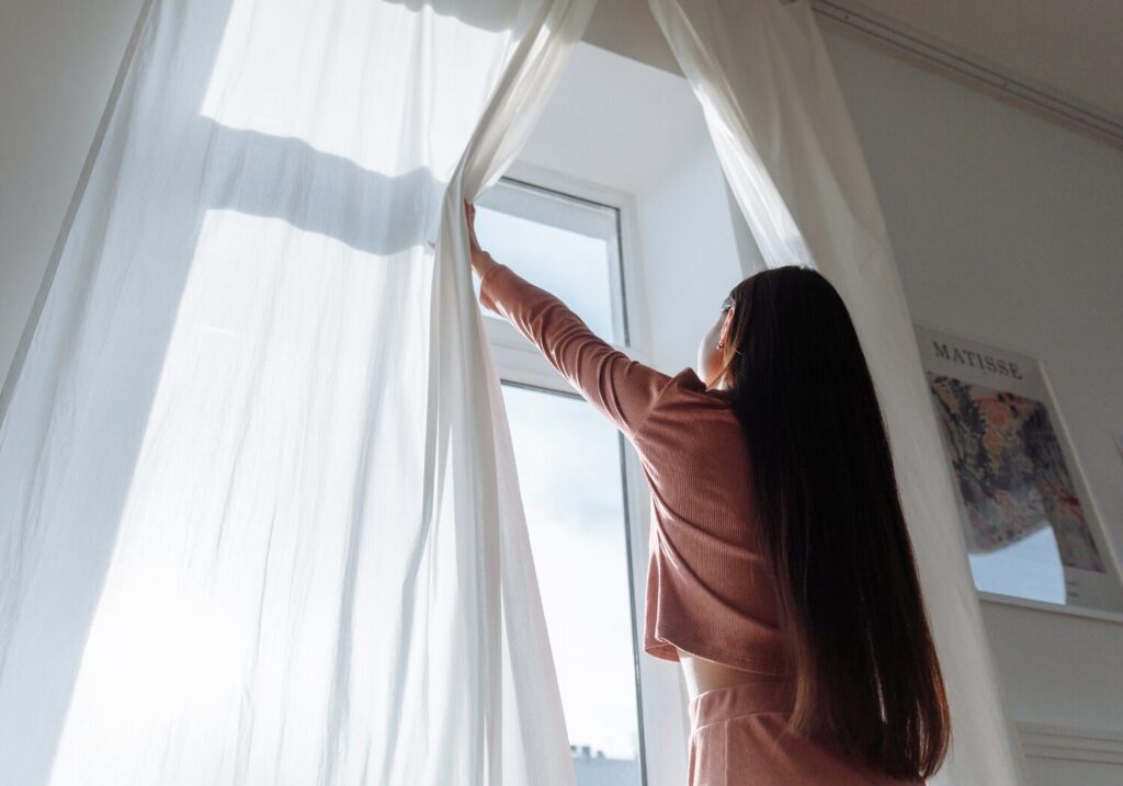 朝のカーテンを開ける女性、太陽の光を浴びながら爽やかな1日のスタート